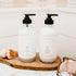 Two bottles with pump dispensers on a wooden tray in a bathroom setting.
