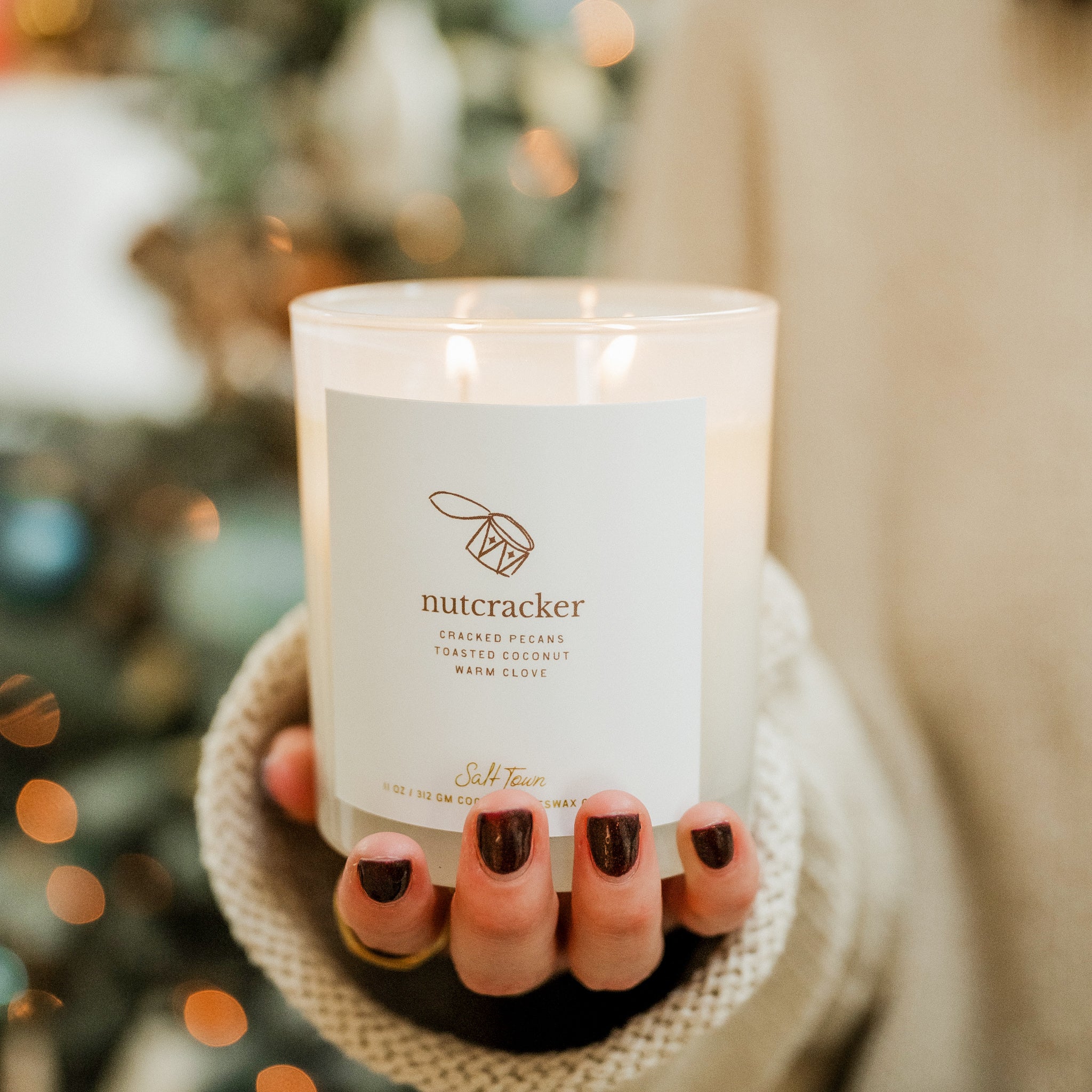 Candle labeled 'nutcracker' held by a person with a blurred Christmas tree in the background