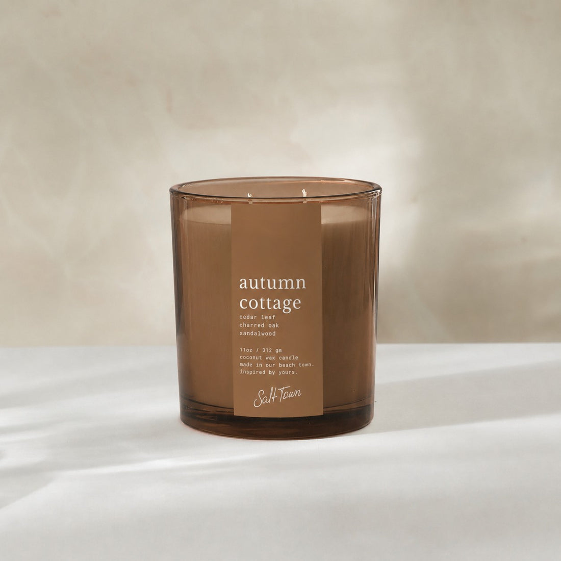 An amber glass jar candle with a brown paper label reading &